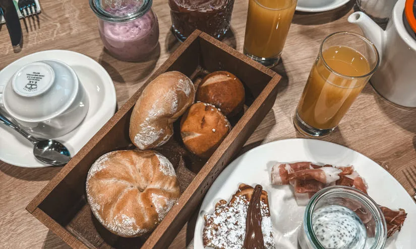 Frühstückstisch mit Gebäck, Marmelade, Getränken und Gläsern