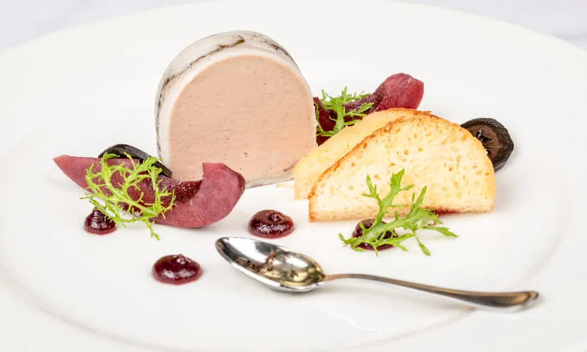 Feine Speise mit Pastete, Brot, Beeren und Kräutern auf weißen Teller.