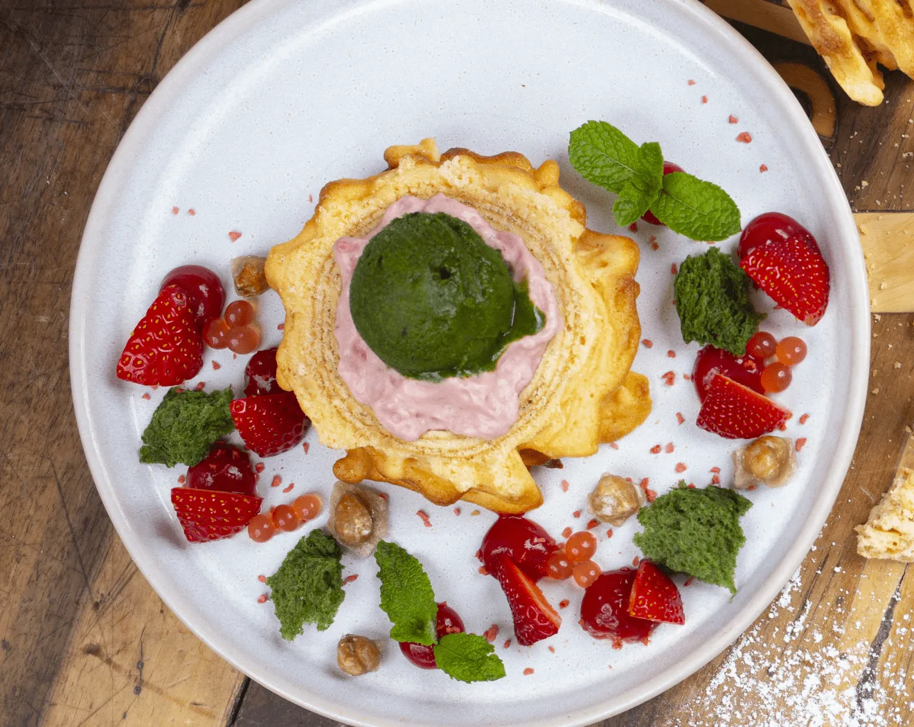 Dessert auf einem Teller mit grüner und rosa Eiscreme, Erdbeeren und Kräutern