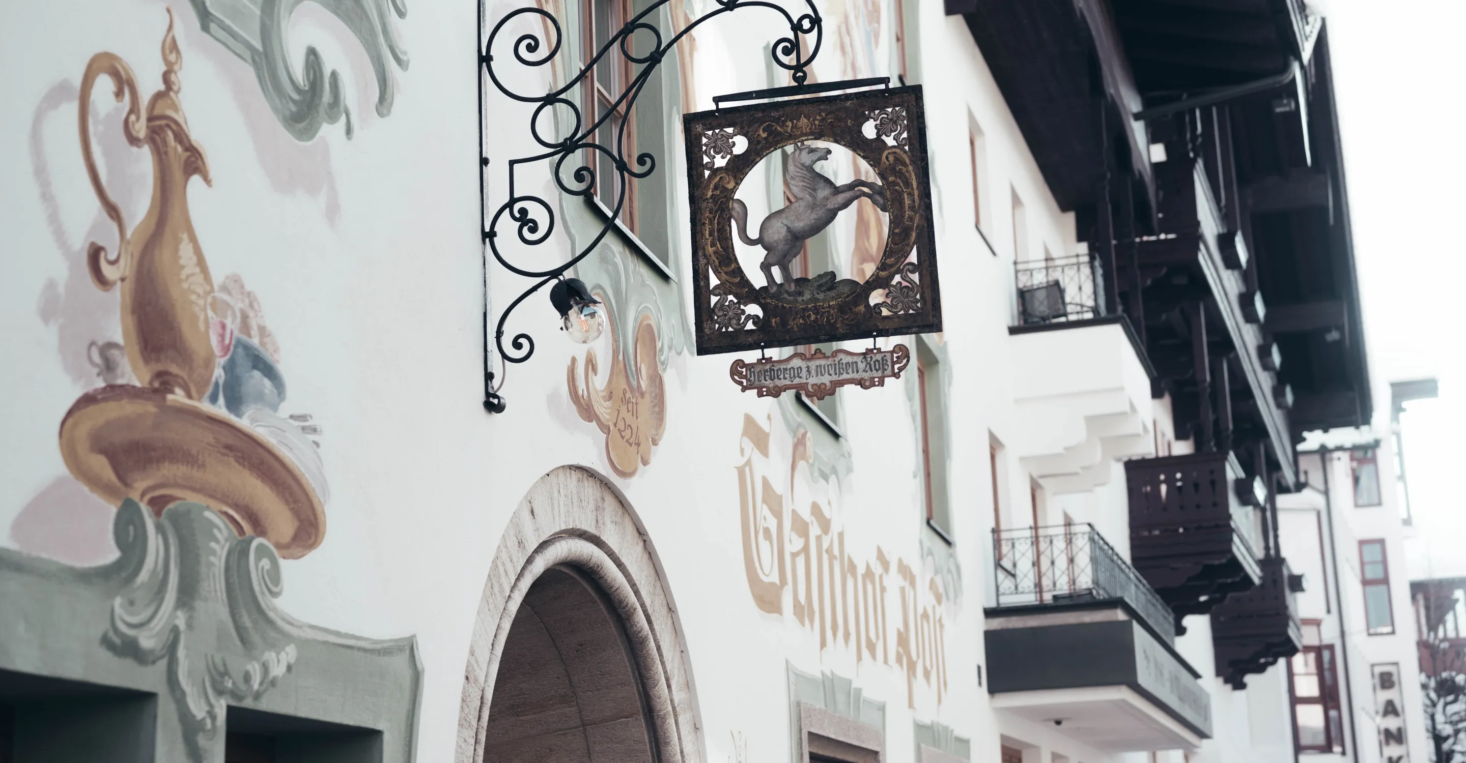 Wandschild mit einem historischen Motiv, umgeben von bemalten Wänden und Balkonen.