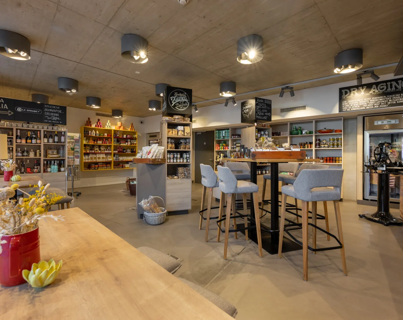 Modernes Café mit Regalen voller Produkte und Sitzgelegenheiten.